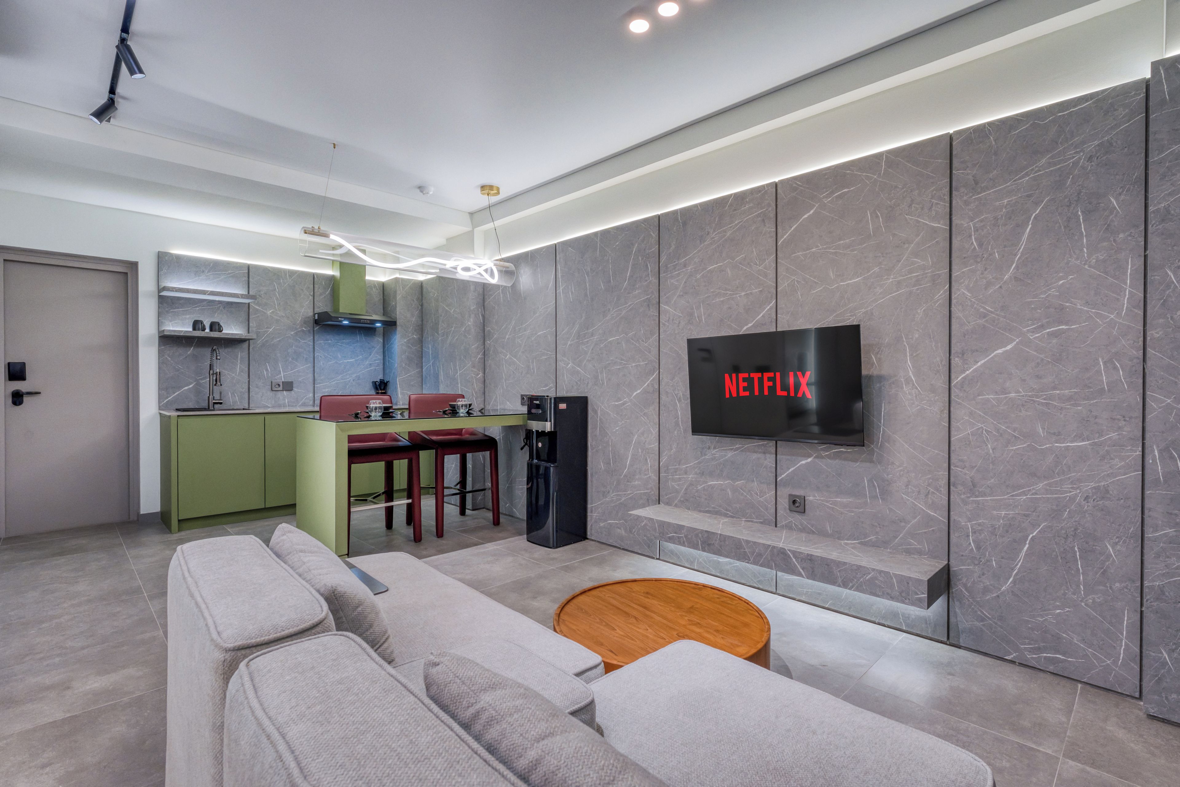 Ein modernes Wohnzimmer mit einem grauen Sofa, einem Holztisch und einem an der Wand befestigten Flachbildfernseher.