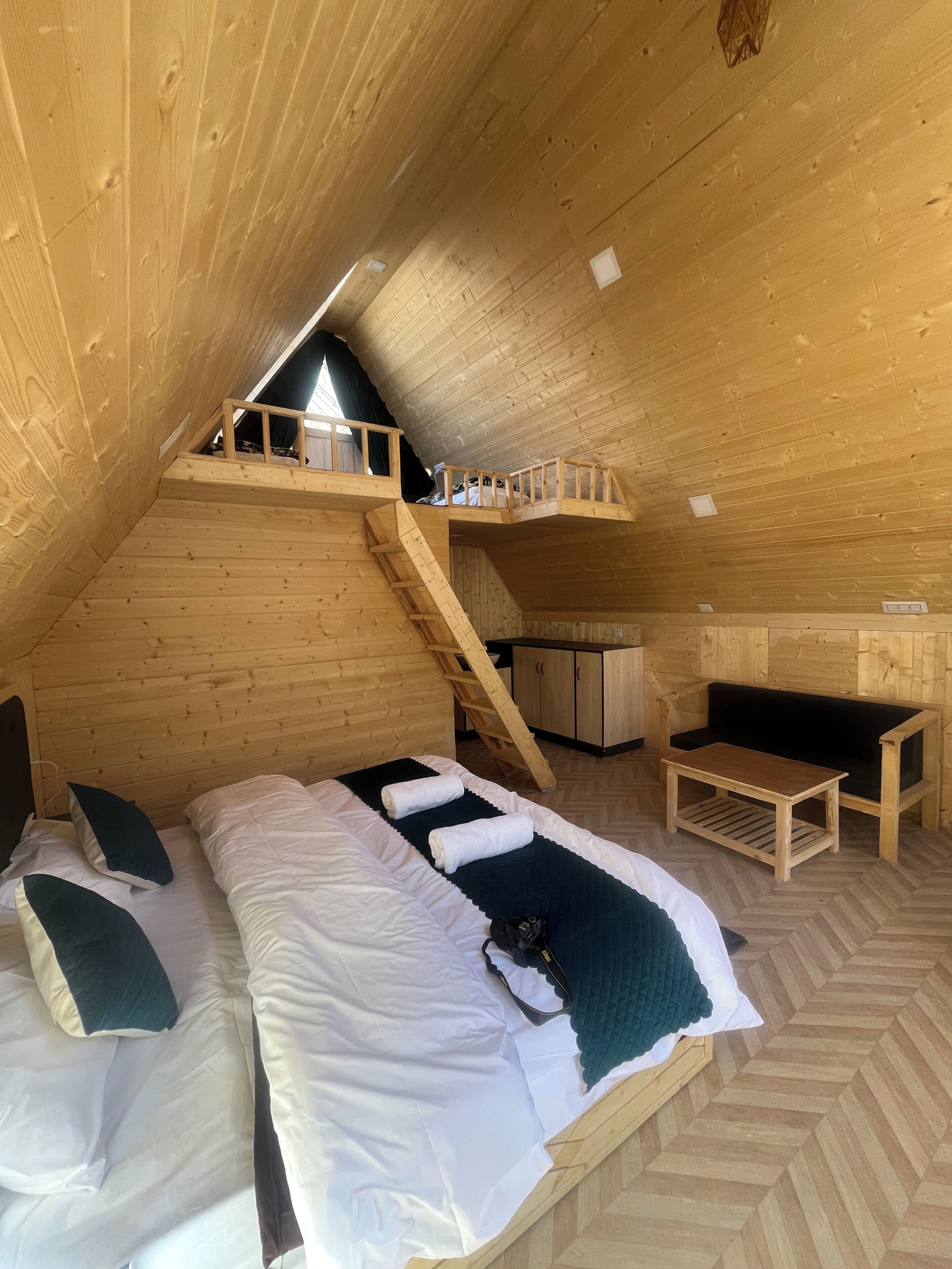 A wooden interior with a loft bedroom, a sofa, a table, and a staircase.