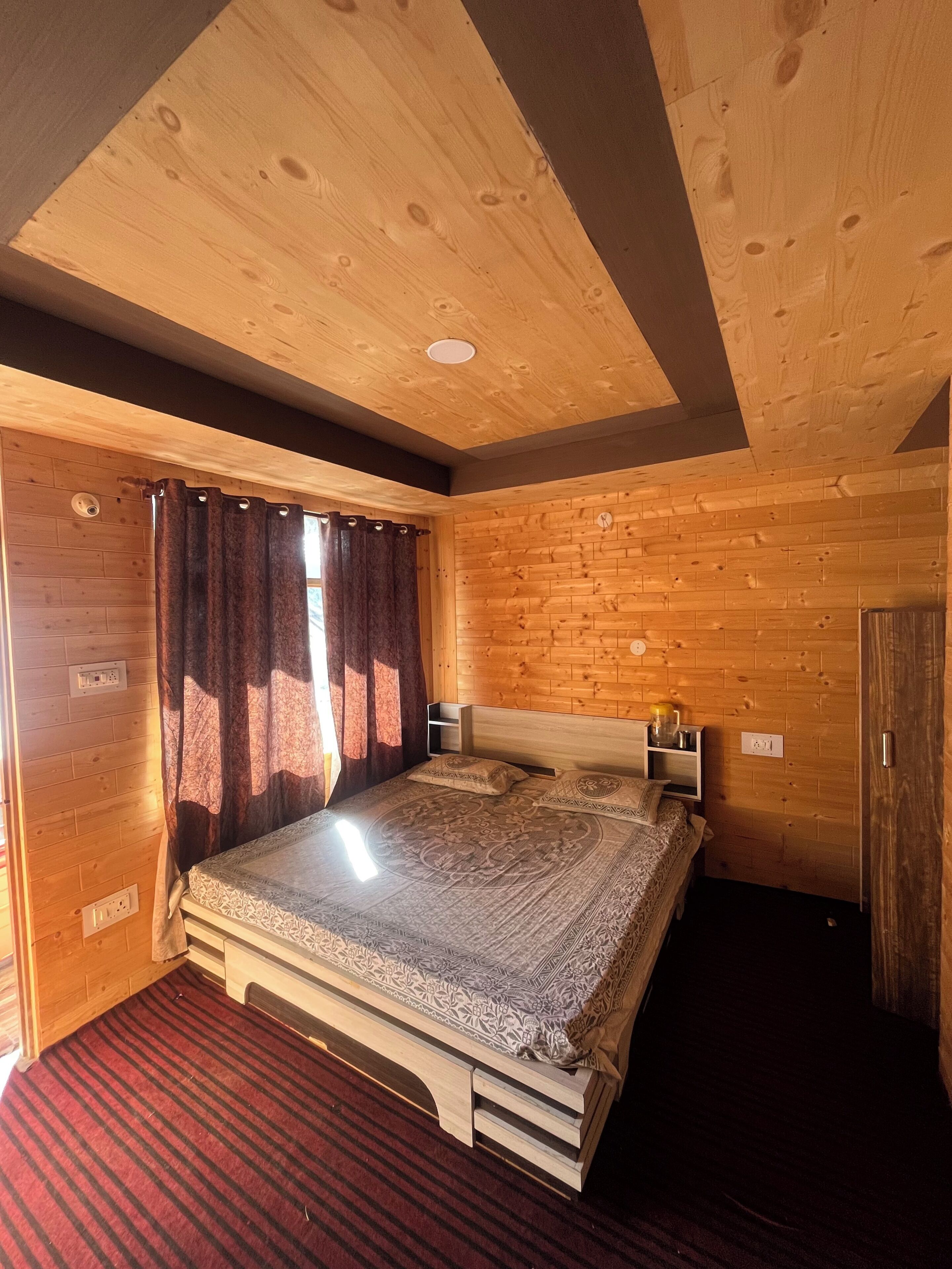A wooden cabin room with a bed, curtains, a bedside table, and a wardrobe.