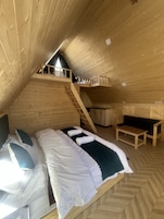 A wooden interior with a loft bedroom, a small table, and a bench.