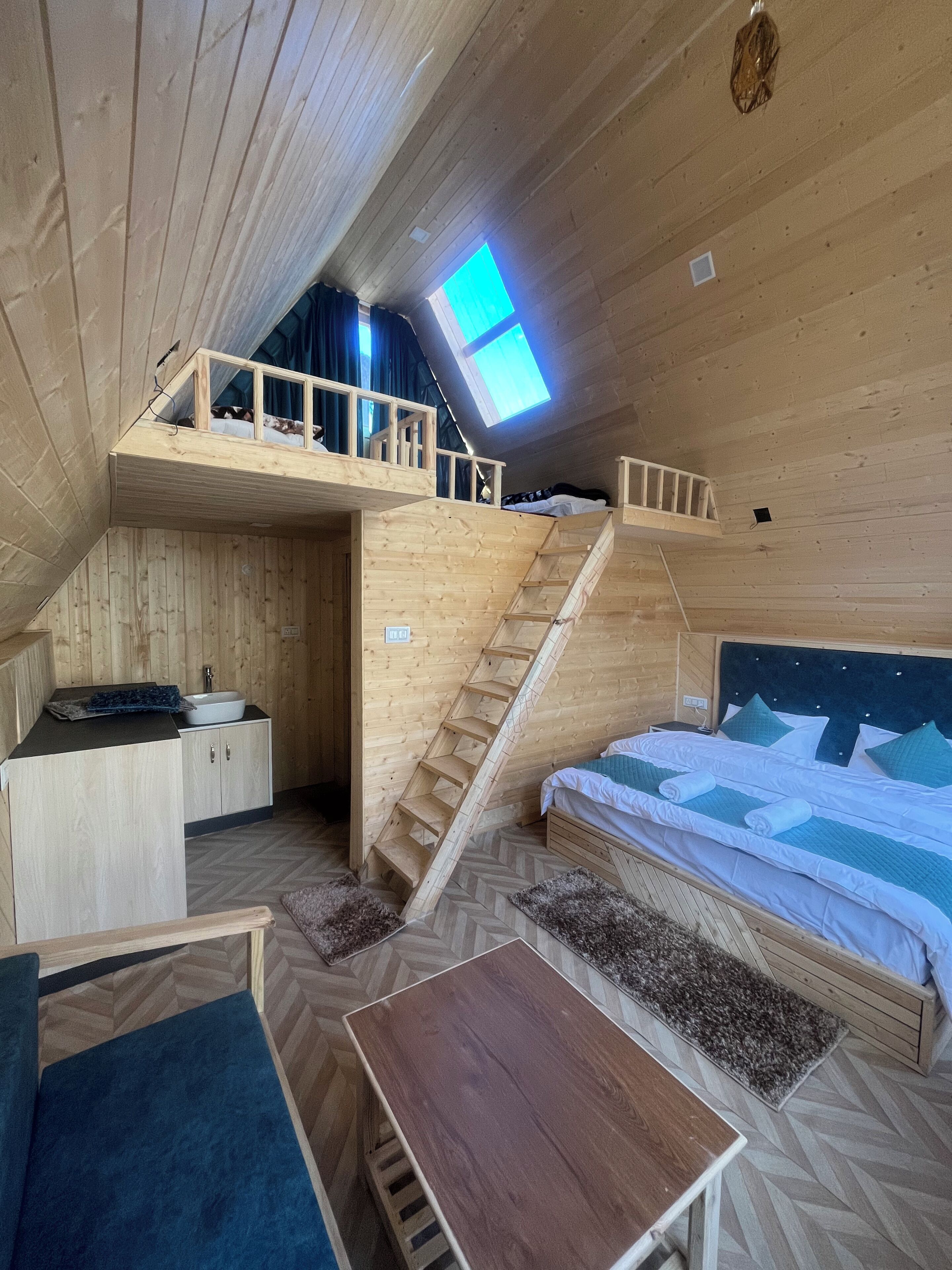Interior de madera con un altillo, una escalera, una pequeña cocina y una mesa.