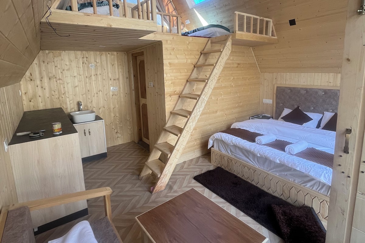 A cozy wooden cabin with a loft bedroom, a small kitchenette, and a staircase leading to the upper sleeping area.