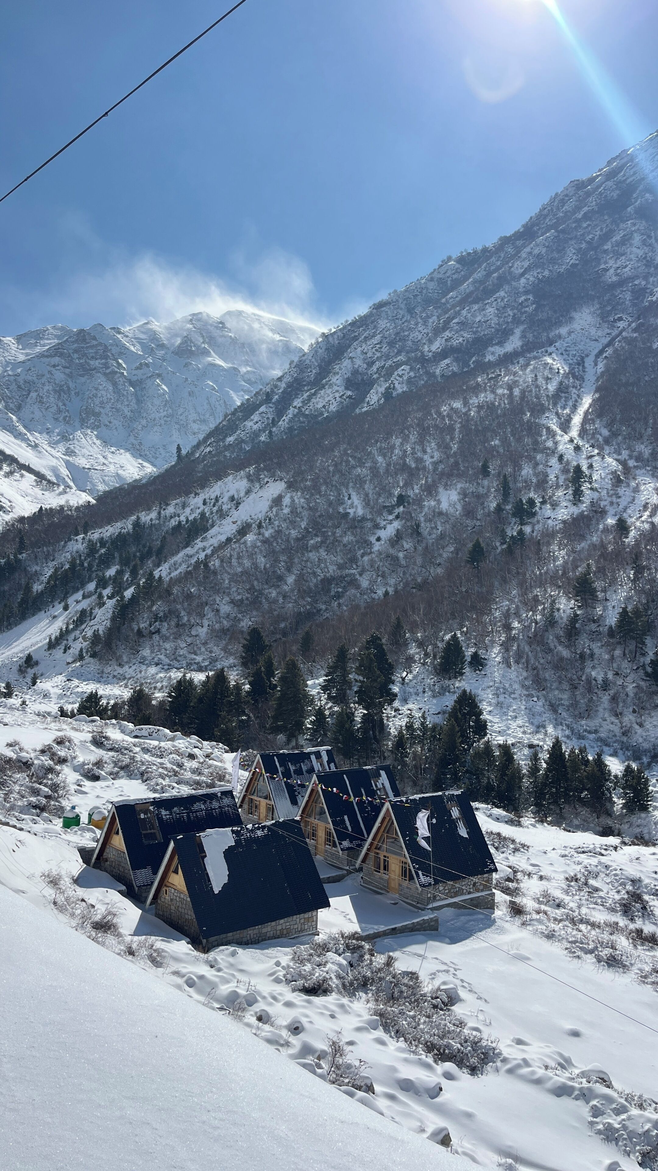 Una fila di chalet con tetti spioventi, sullo sfondo di montagne innevate e cielo sereno.