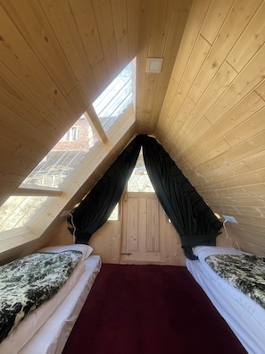A small attic bedroom with two beds, a red carpet, wooden walls, and a sloped ceiling with skylights. - The Grand Lamkhaga By Mountain Bee (Chitkul)