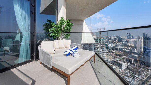 Un balcone con divano, cuscini, una pianta in vaso e vista su un panorama urbano con edifici e lavori in corso.