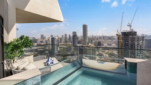 Una piscina a sfioro sul tetto con vista sulla città, un’area relax con divano e cuscini, e una ringhiera in vetro.