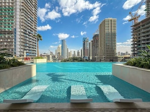 Piscina com águas cristalinas, rodeada por edifícios altos e palmeiras.