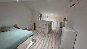 Ett sovrum med en säng, ett litet sängbord, ett träräcke och utsikt över ett kök och en balkong.