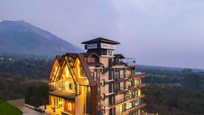 A modern multi-story hotel with a unique triangular facade, multiple balconies, and a view of a mountainous landscape. - Sterling Nirmaya Dharamshala (Dharamshala)