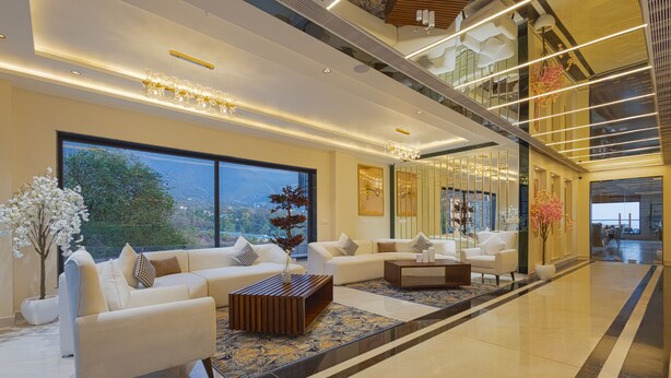A spacious lobby with a modern design, featuring a large seating area with sofas and a coffee table, large windows offering a view of the outdoors, and a polished floor. - Sterling Nirmaya Dharamshala (Dharamshala)