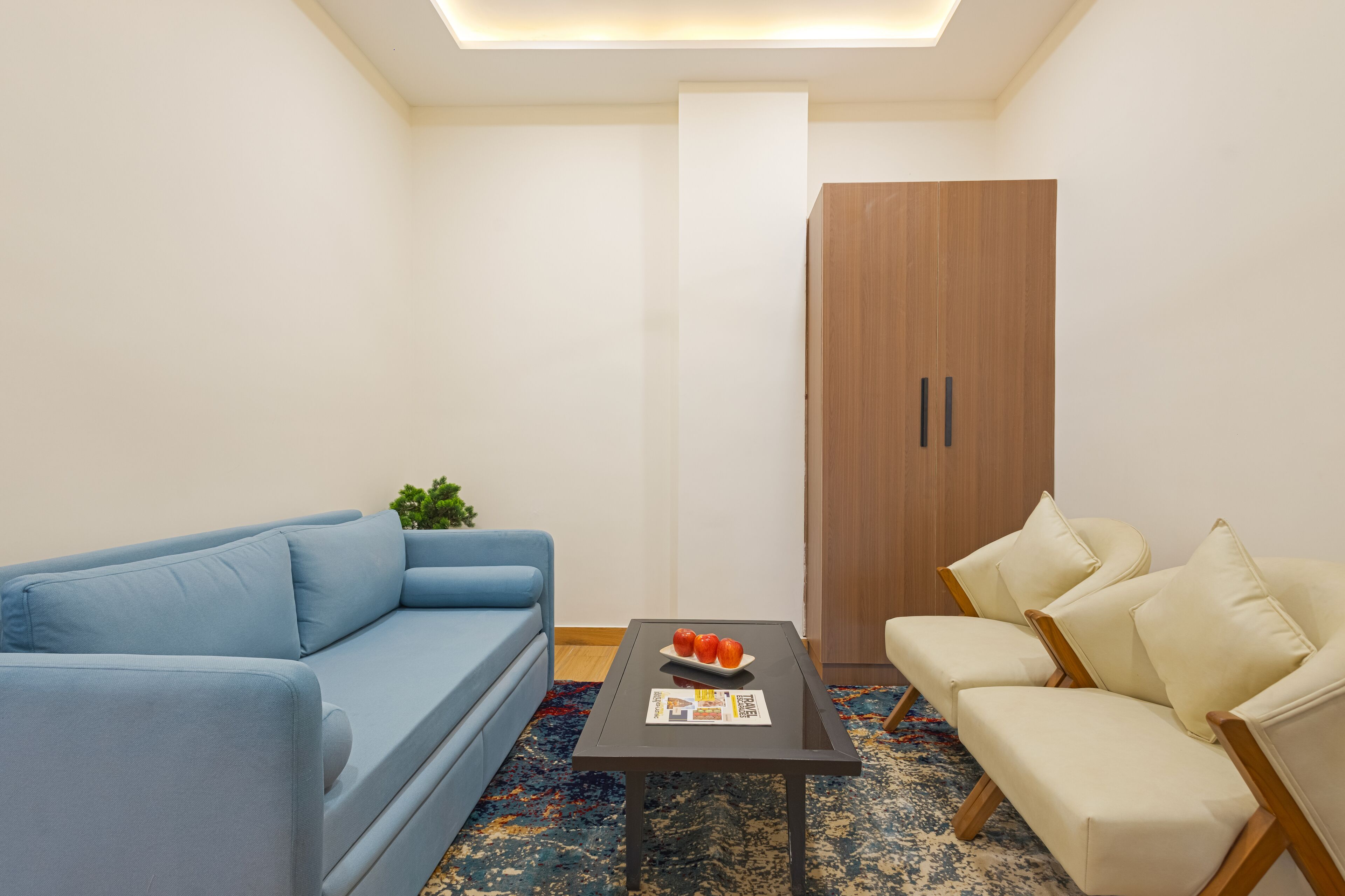 Een moderne woonkamer met een blauwe bank, een beige fauteuil, een salontafel met een tijdschrift en appels, en een houten garderobe.