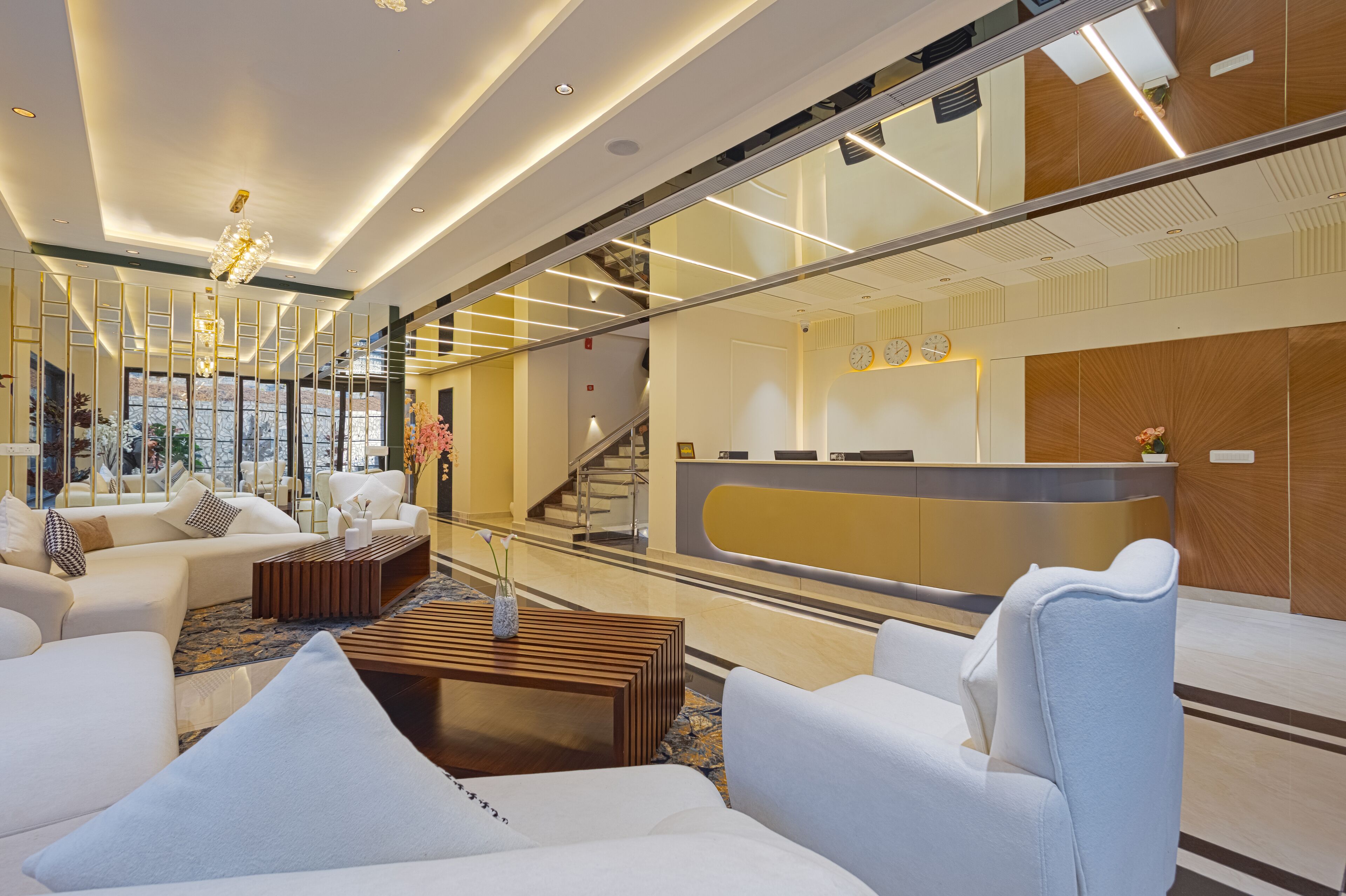A modern hotel lobby with a reception desk, seating area with sofas, and a staircase.