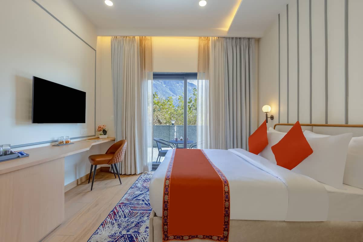 Hotelkamer met een bed, bureau, televisie, balkon met uitzicht en raam met gordijnen.
