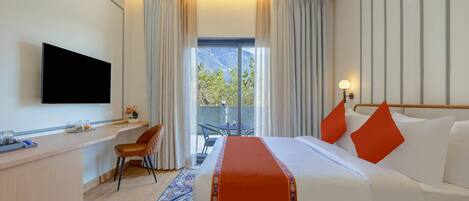 Habitación de hotel con cama, escritorio, televisión, balcón con vistas y ventana con cortinas.
