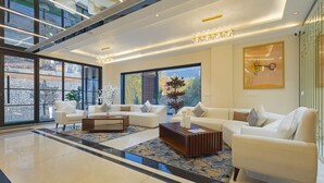 A spacious living area with a large window, a chandelier, and a modern coffee table. - Sterling Nirmaya Dharamshala (Dharamshala)