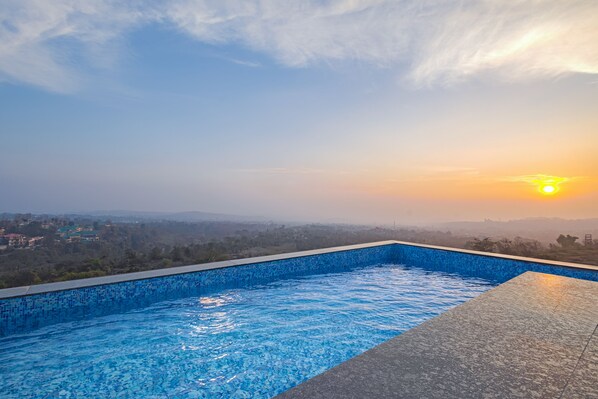 Une piscine offrant une vue sur un coucher de soleil se dégageant sur un paysage lointain.