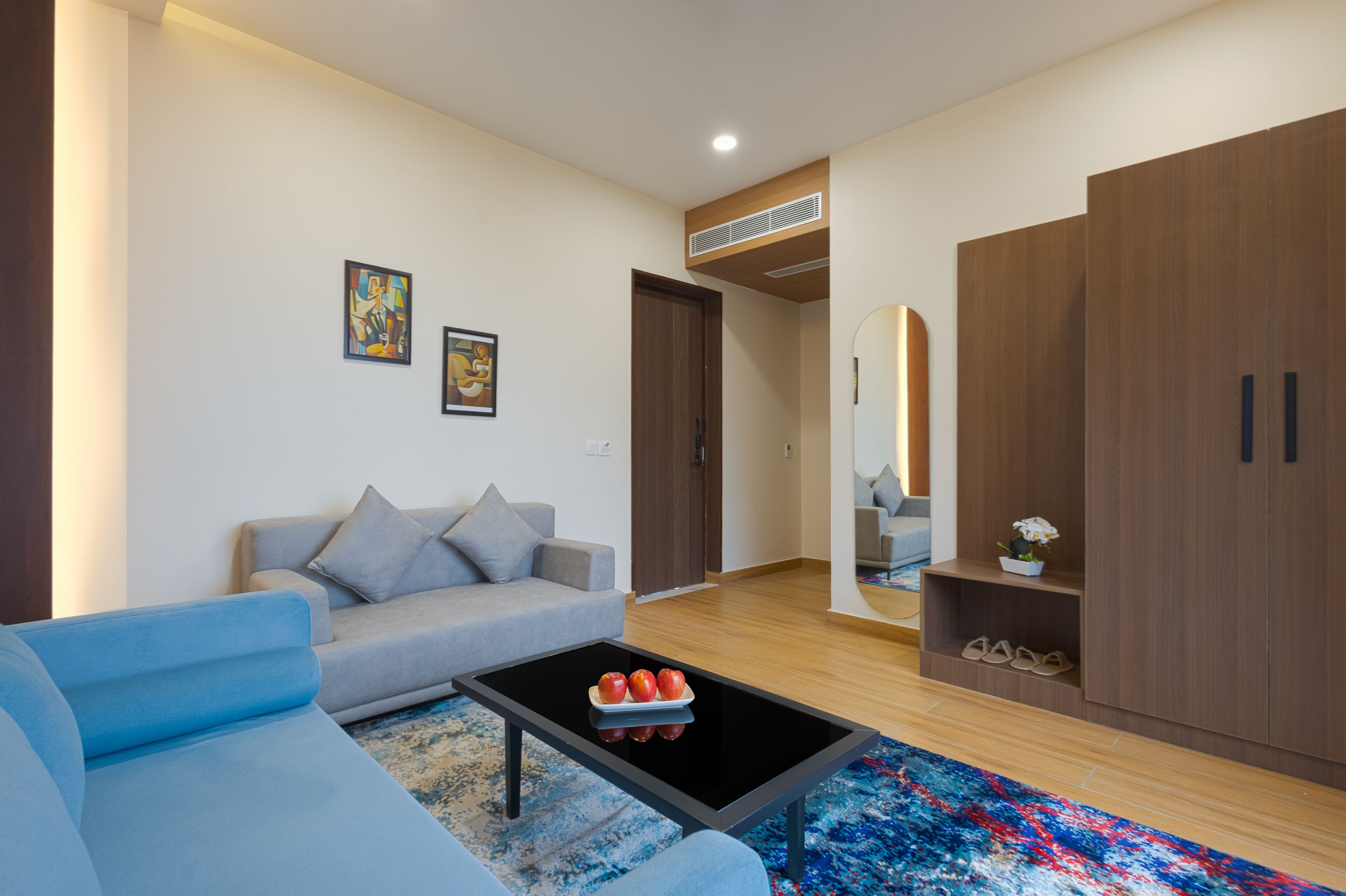 A modern living room with a sofa, a coffee table with apples, a blue rug, and wooden flooring.