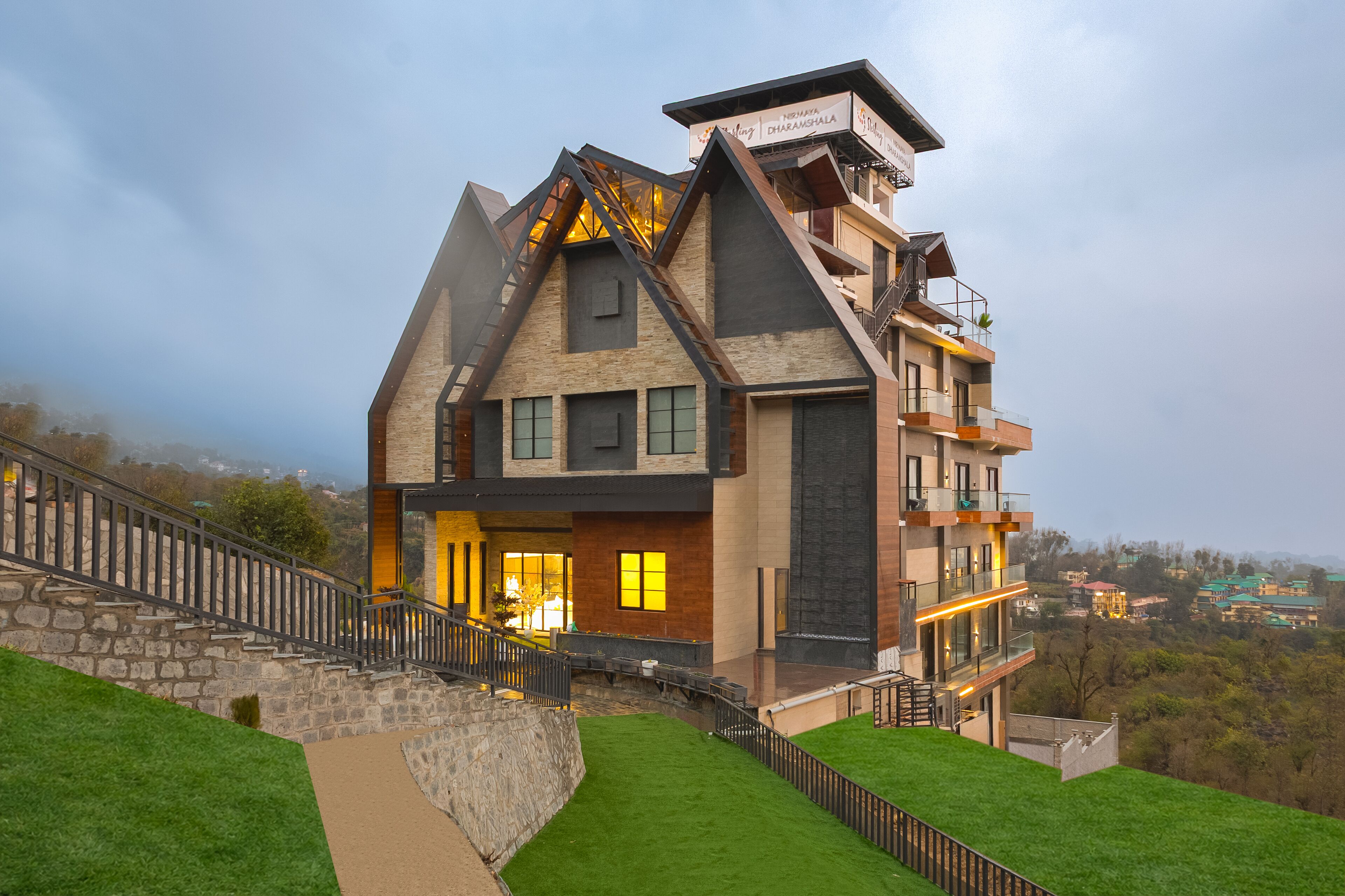 Una casa moderna de varios pisos con una escalera de piedra, un césped cuidado y vistas del paisaje circundante.