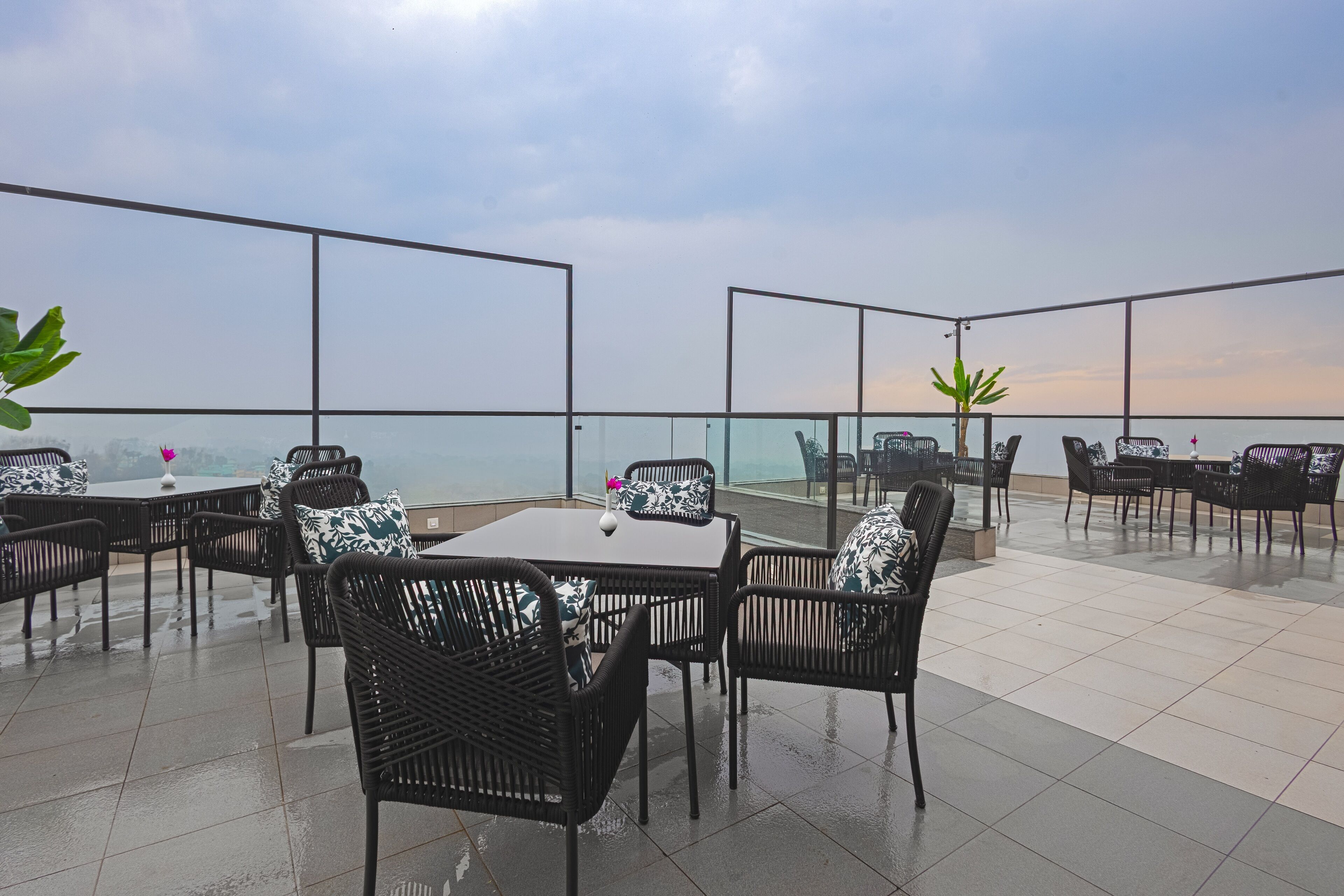 An outdoor terrace with tables and chairs, a glass railing, and a view of the sea.