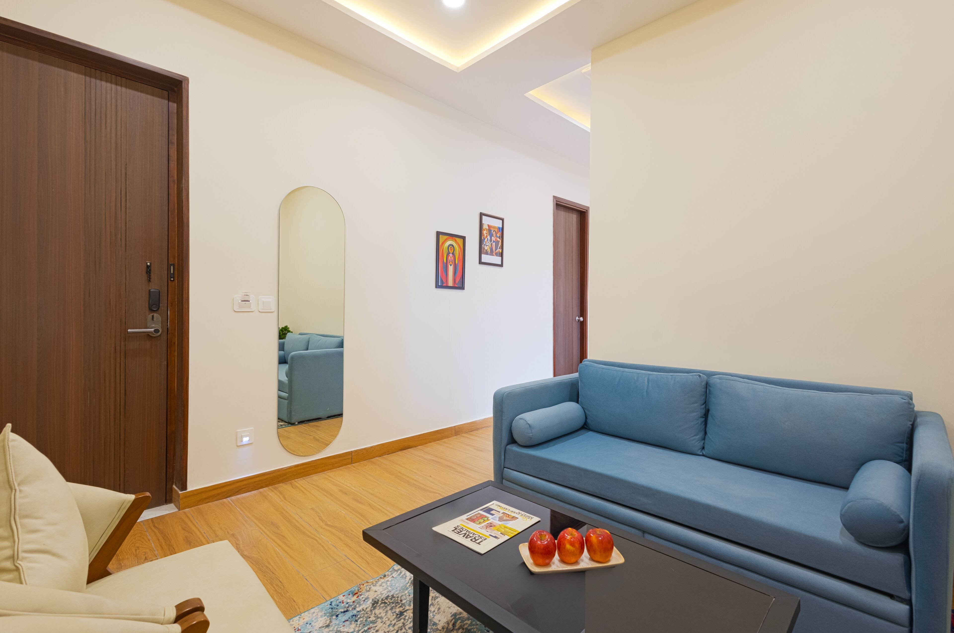 A modern living room with a blue sofa, a wooden floor, a small table with apples, and a door.