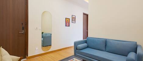 A modern living room with a blue sofa, a wooden floor, a small table with apples, and a door.