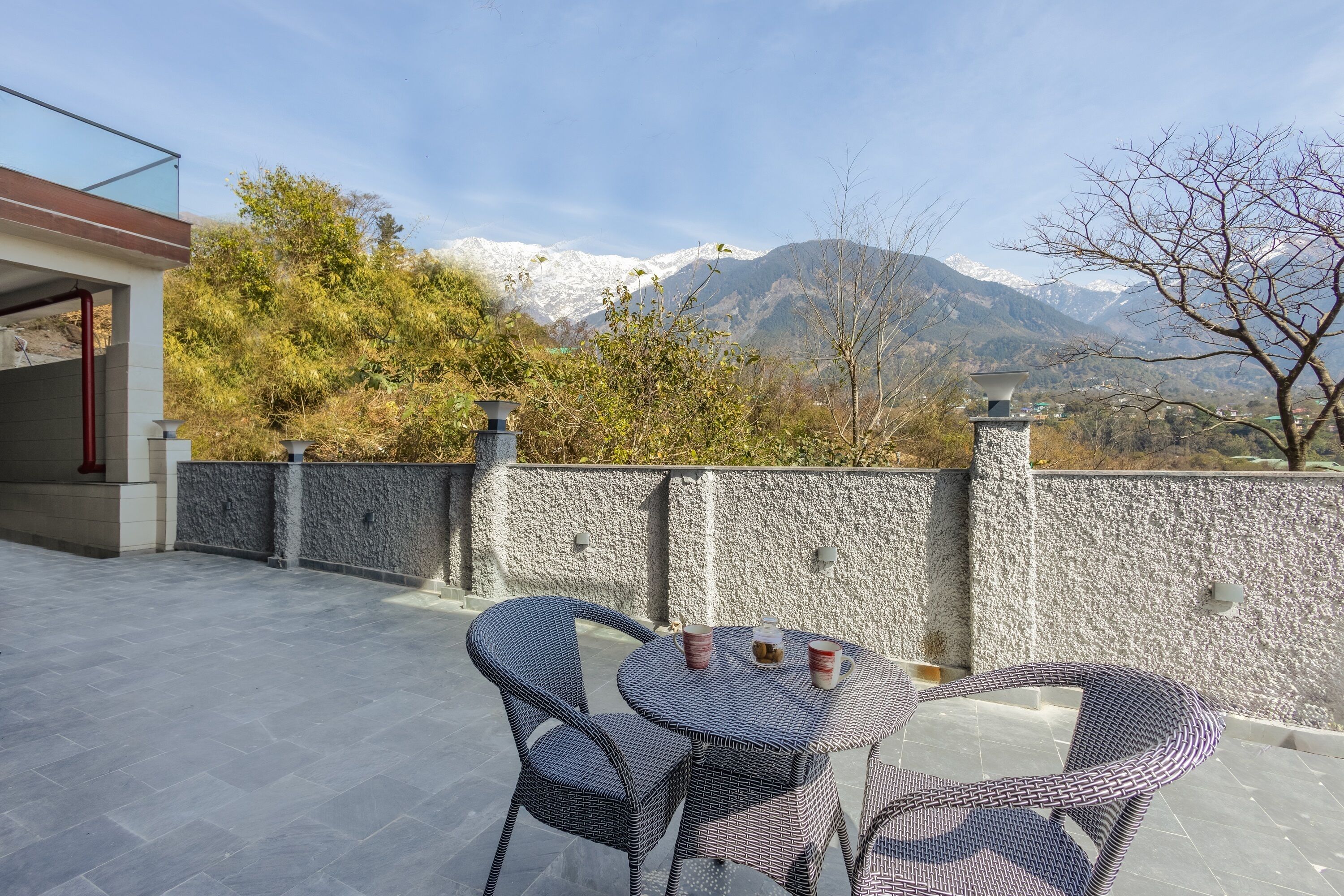 A terrace with a table and chairs, a stone wall, and a view of snow-capped mountains.