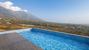 A swimming pool with a view of a mountainous landscape and a village in the background. - Sterling Nirmaya Dharamshala (Dharamshala)