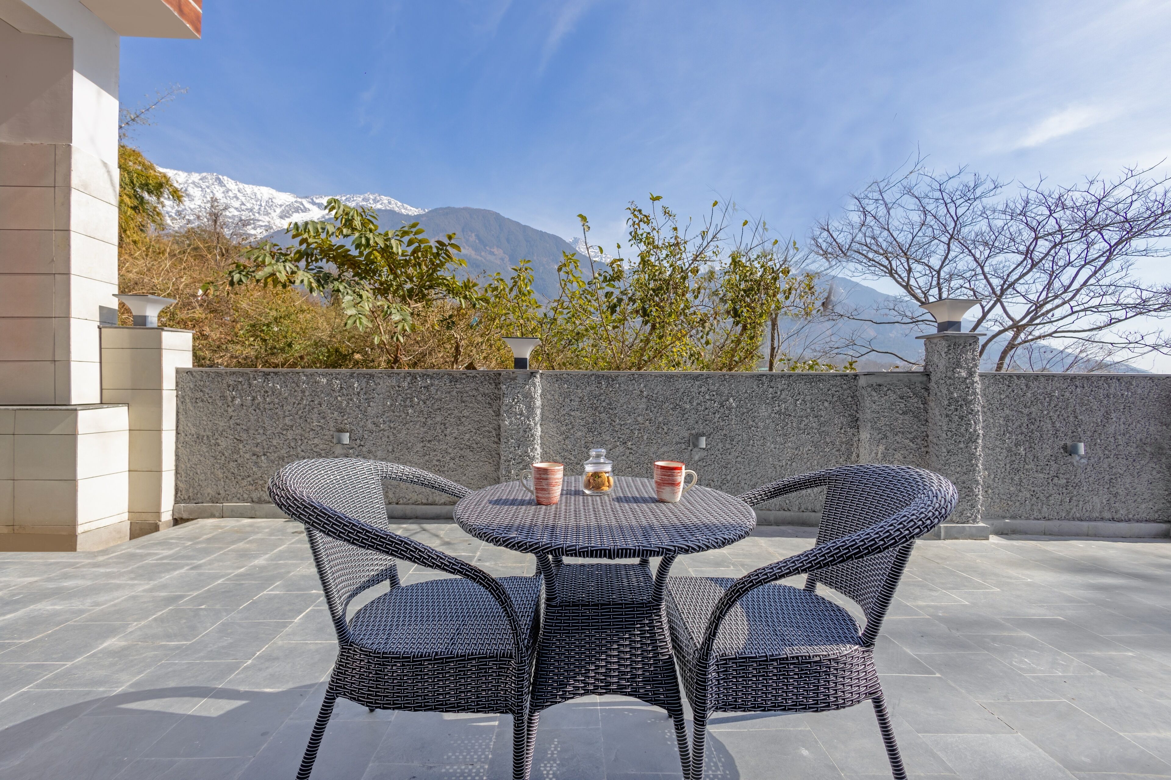 A patio with wicker chairs and a table, a water feature, and a view of snow-capped mountains.