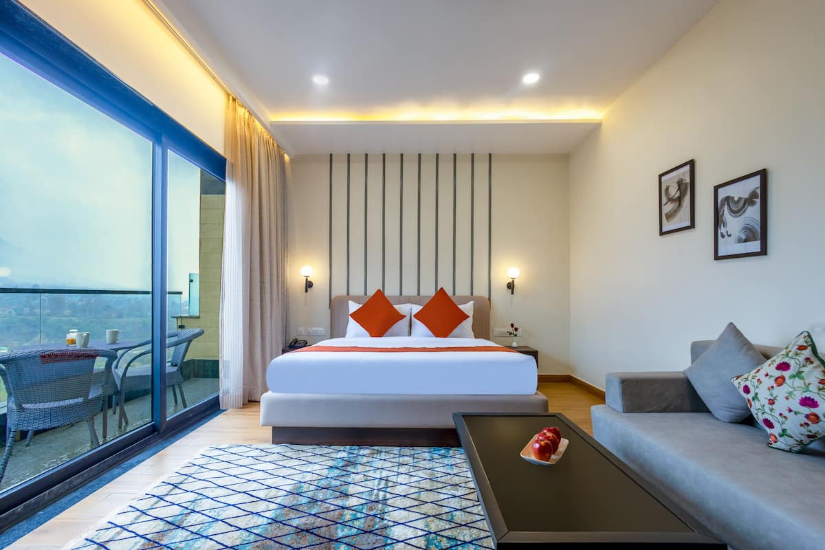 Hotelkamer met een groot bed, een bank, een salontafel en een balkon met een eethoek.