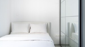 Un dormitorio minimalista con cama, ropa de cama blanca y un muro espejado.