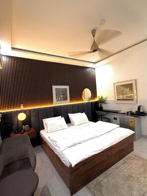 A modern hotel room with a large bed, a desk, a chair, a small kitchenette, and a ceiling fan. - Villa Hills Hotel  (Senya Beraku)
