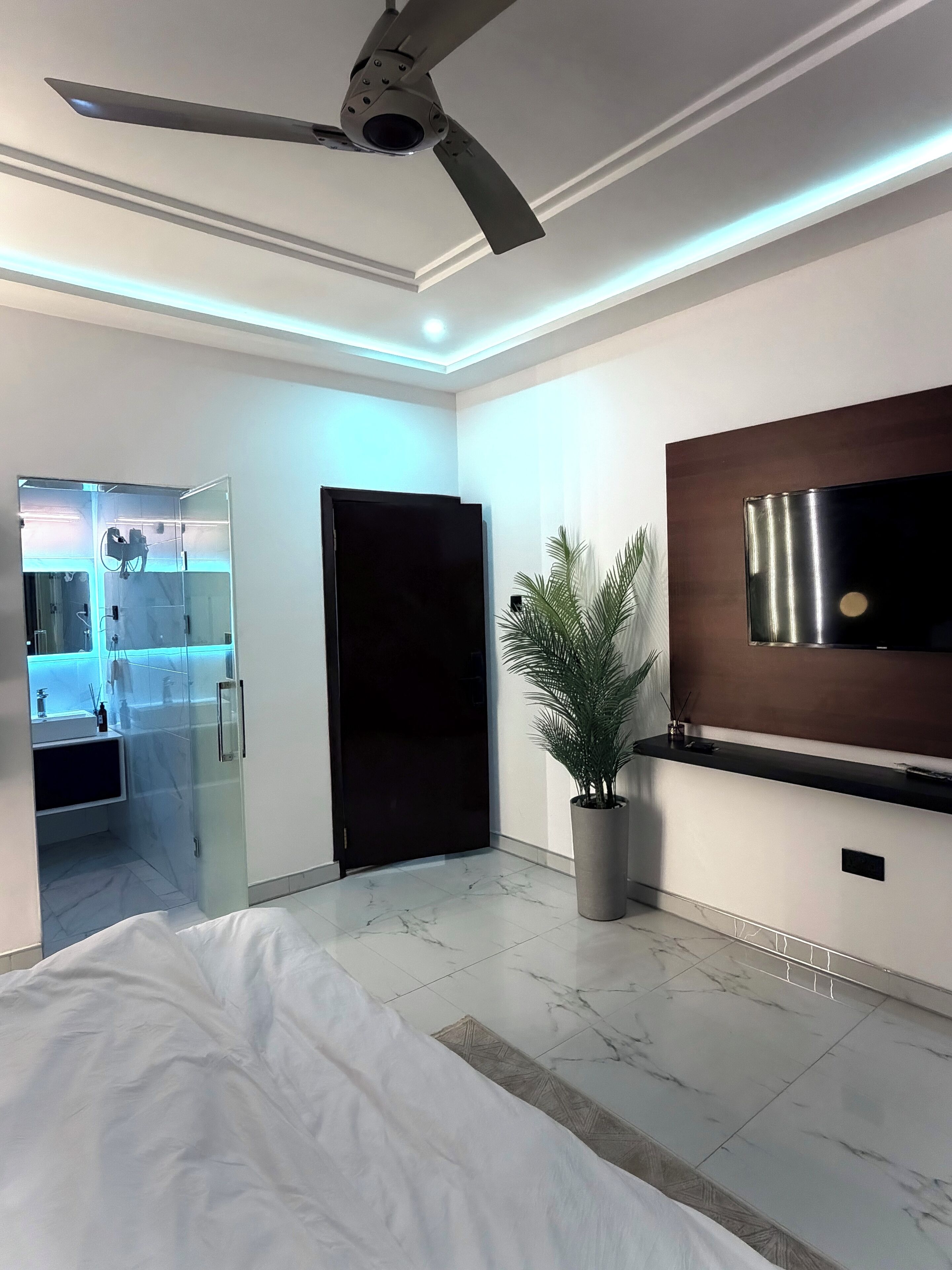 Une chambre à coucher moderne avec un lit, un ventilateur de plafond, un téléviseur fixé au mur et une plante en pot.