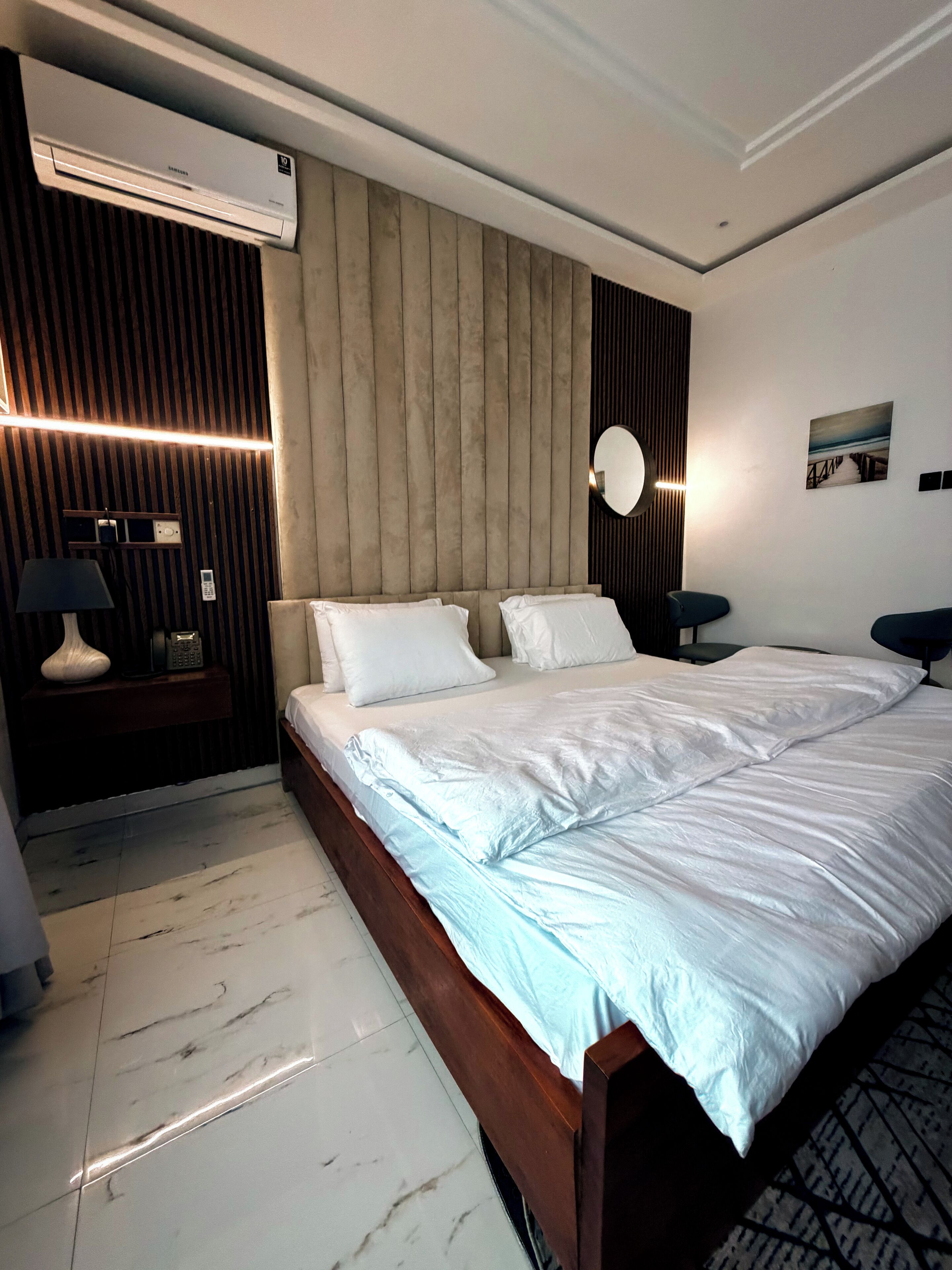 Een moderne hotelkamer met een groot bed, een ingebouwde airconditioning, een nachtkastje met een lamp en een wandspiegel.