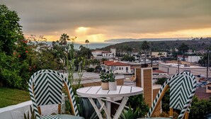 A terrace with two chairs and a table, overlooking a coastal town with buildings and palm trees.