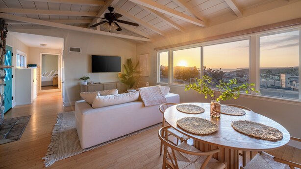 A spacious living room with a white sofa, wooden dining table, and a large window with a city view.