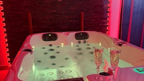 A hot tub with two glasses of champagne, red ambient lighting, and a brick wall background. - Émoi de Toi – Love Room Prestige, Private Jacuzzi, Breakfast (Sigean)