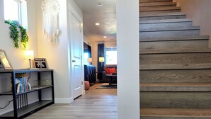 Un couloir avec un escalier en bois, une bibliothèque et un attrape-rêves accroché au mur.