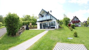 Ett modernt hus i två våningar med en balkong, en asfalterad uppfart och en liten trädgårdsyta.