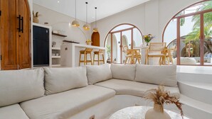 Un salon moderne avec un canapé d’angle beige, une table basse ronde ornée d’un vase, et un coin repas avec des chaises et une table en bois.