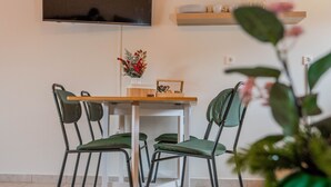 Un'area pranzo con un tavolo in legno, sedie verdi, una TV a schermo piatto montata a parete ed scaffali con bicchieri e oggetti decorativi.