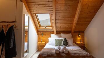 Une chambre confortable avec un plafond en pente, un lit avec des oreillers et une couverture, une table de chevet avec une lampe et un porte-manteau avec une veste.