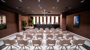 A conference room with rows of chairs facing a reception desk, large windows, and a ceiling with recessed lighting.