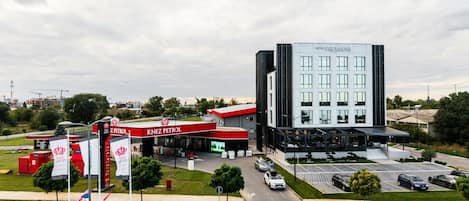 A hotel with a modern design, a parking lot, and a nearby gas station.