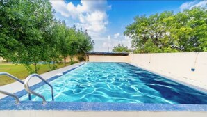 Una piscina rectangular con agua azul cristalina, rodeada por un muro blanco y una escalera metálica.