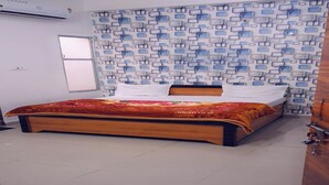Un dormitorio con cama de madera, papel tapiz estampado, pared blanca y una ventana.
