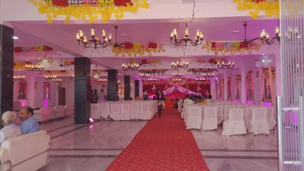 Un amplio salón con alfombra roja, mesas y sillas blancas, decorado con candelabros y arreglos florales.