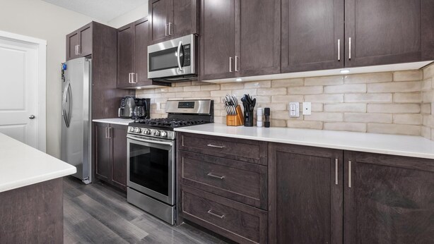Una cocina moderna con armarios de madera oscura, electrodomésticos de acero inoxidable y encimera blanca.