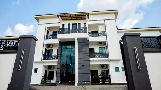 A modern multi-story building with a central entrance, balconies, and a logo at the bottom. - Bosanic Hotel And Suites (Benin City)