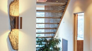 Ein modernes Interieur mit einer Wandverkleidung aus Holz, einer Treppe mit Glasgeländer und einer Tür zu einem weiteren Raum.