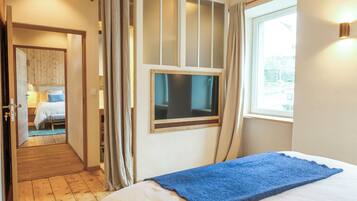 A bedroom with a bed, a window with curtains, a TV mounted on the wall, and a wooden floor.